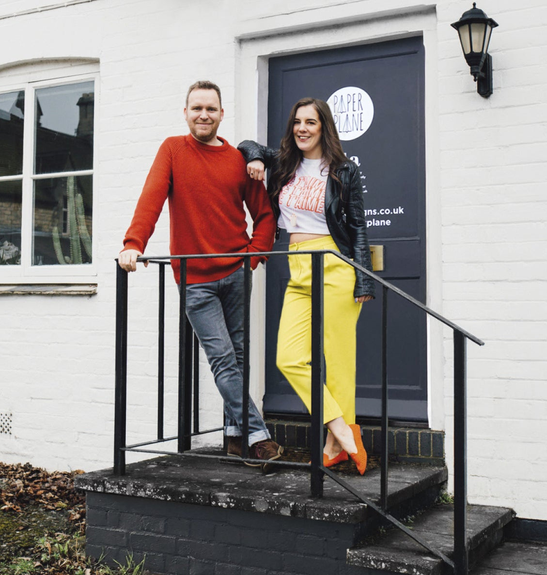 Two people standing on a black metal staircase in front of a white building with a door.