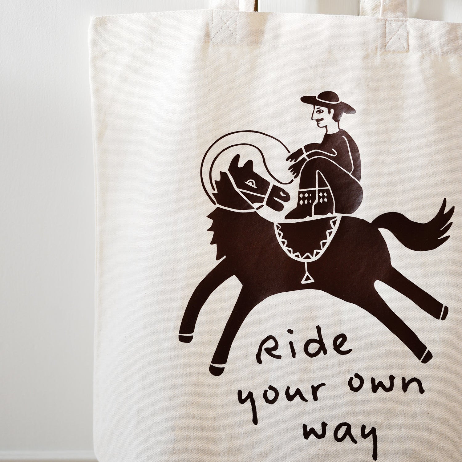 Tote bag with a graphic of a person riding a horse and the text 'Ride your own way' on a white background.