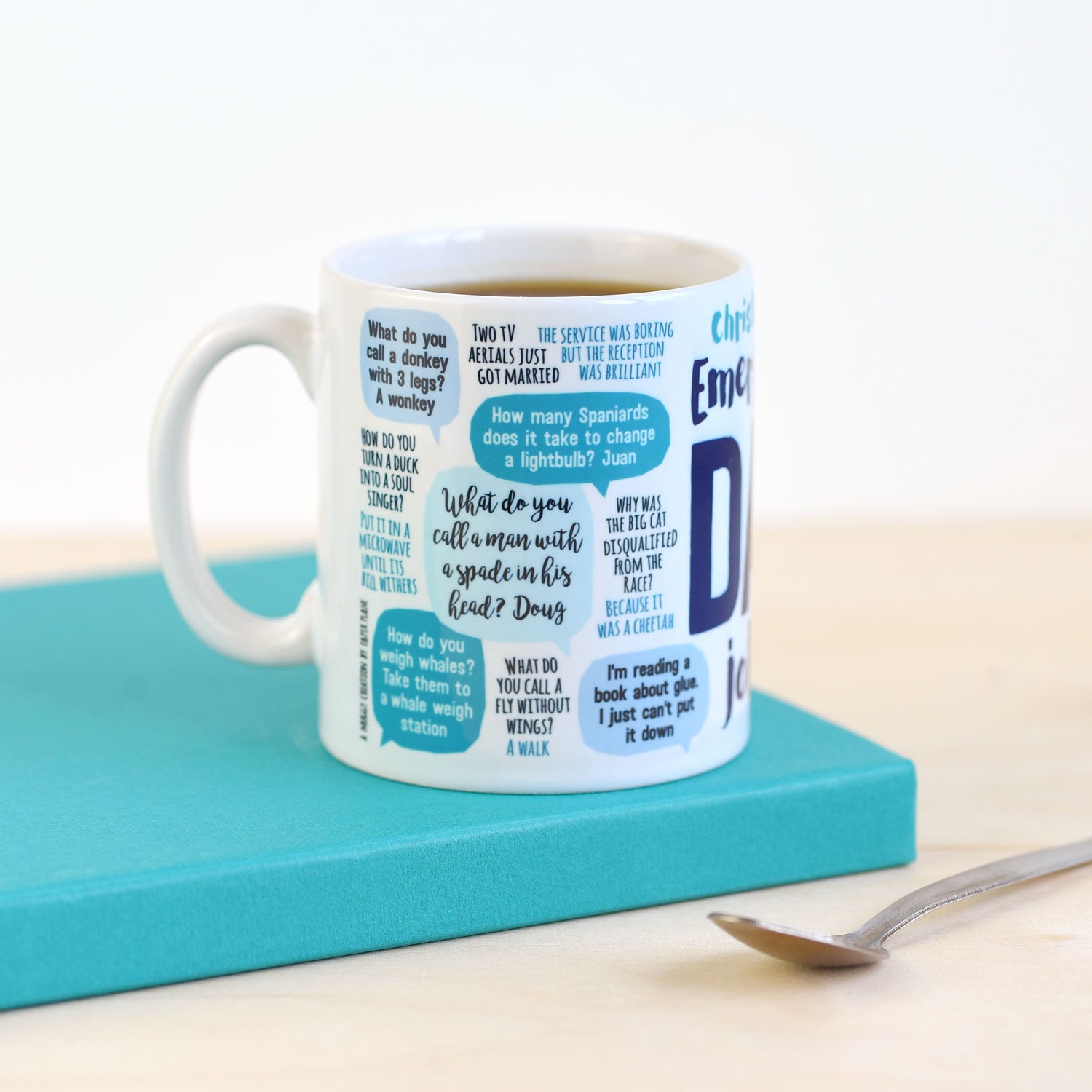 White mug with blue text on a teal coaster with a spoon