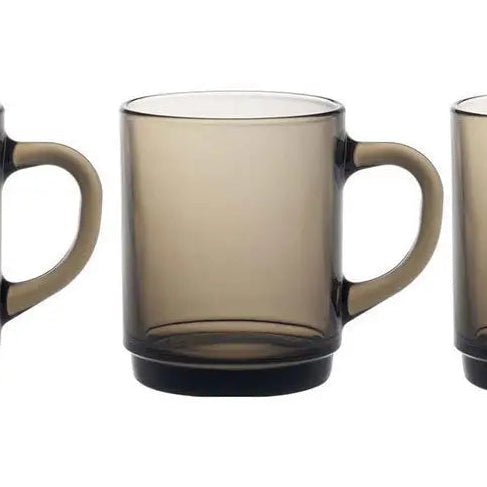A translucent smoky brown glass mug with a matching handle, shown against a plain white background with other cropped mugs partially visible on the left and right.